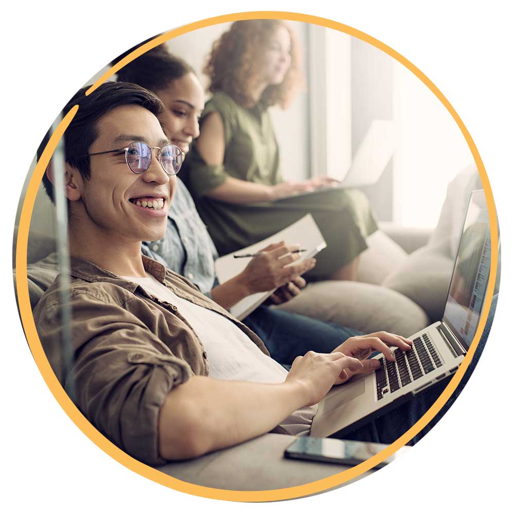 Young Asian man with glasses smiling and looking away from his laptop